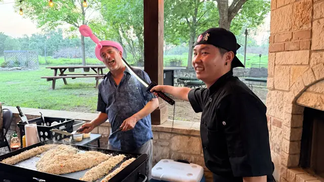 A guest in a balloon hat laughs as the chef points a toy katana