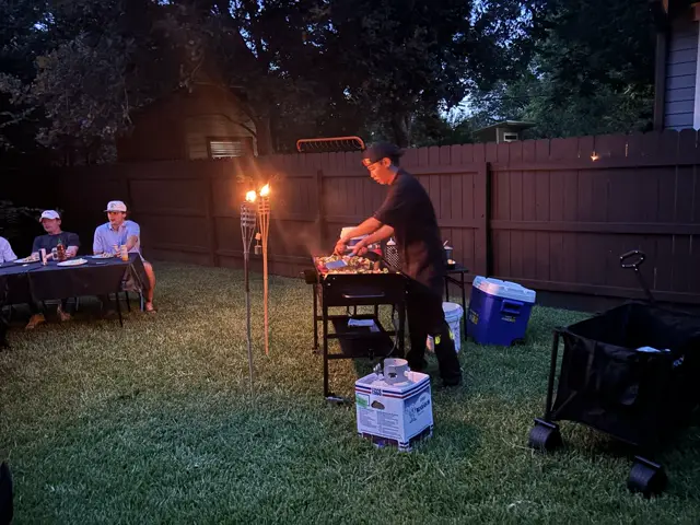 The chef cooks on the teppan by tiki-torch light at an evening backyard party